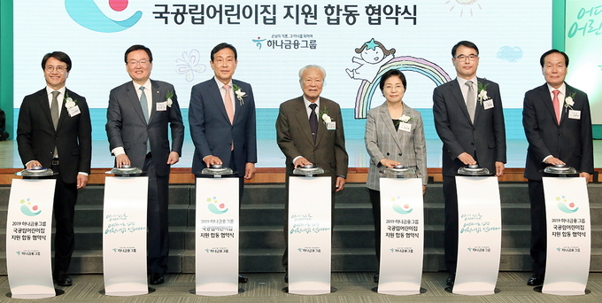 하나금융은 9일 서울 중구 을지로 하나금융 사옥에서 국공립어린이집 지원사업 대상지로 선정된 23개 지자체와 국공립어린이집 지원을 위한 합동 업무협약을 체결했다. 협약식에 참석한 관계자들이 기념 세레모니를 하고 있는 모습. (사진 왼쪽부터 이재현 인천 서구청장, 문인 광주 북구청장, 김정태 하나금융 회장, 박승 하나금융 사회공헌위원회 위원장, 김미경 서울 은평구청장, 장충남 경남 남해군수, 김주수 경북 의성군수) Photo @ 하나금융그룹