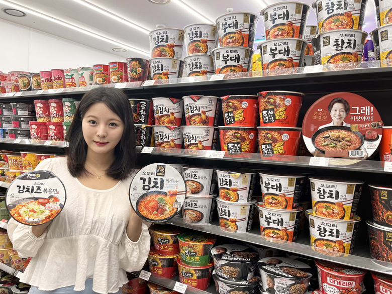 GS25에서 모델이 '오모리김치즈볶음면'과 '오모리김치찌개라면'을 들고 포즈를 취하고 있는 모습. 사진ㅣGS리테일